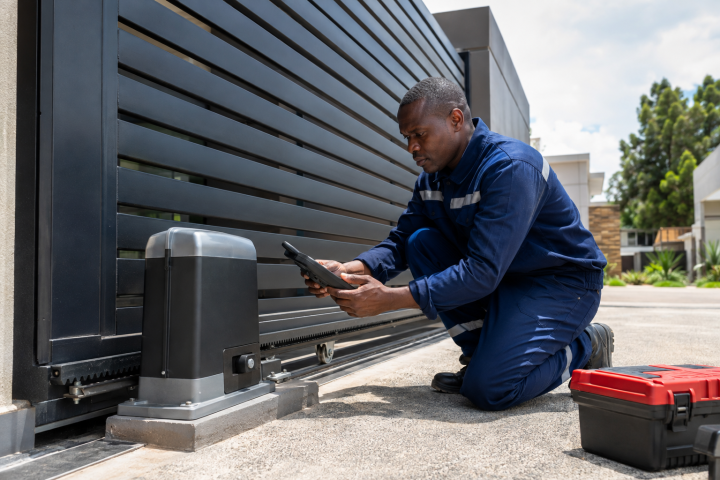 Technician checking a sliding gate motor and rack on a Kenyan driveway